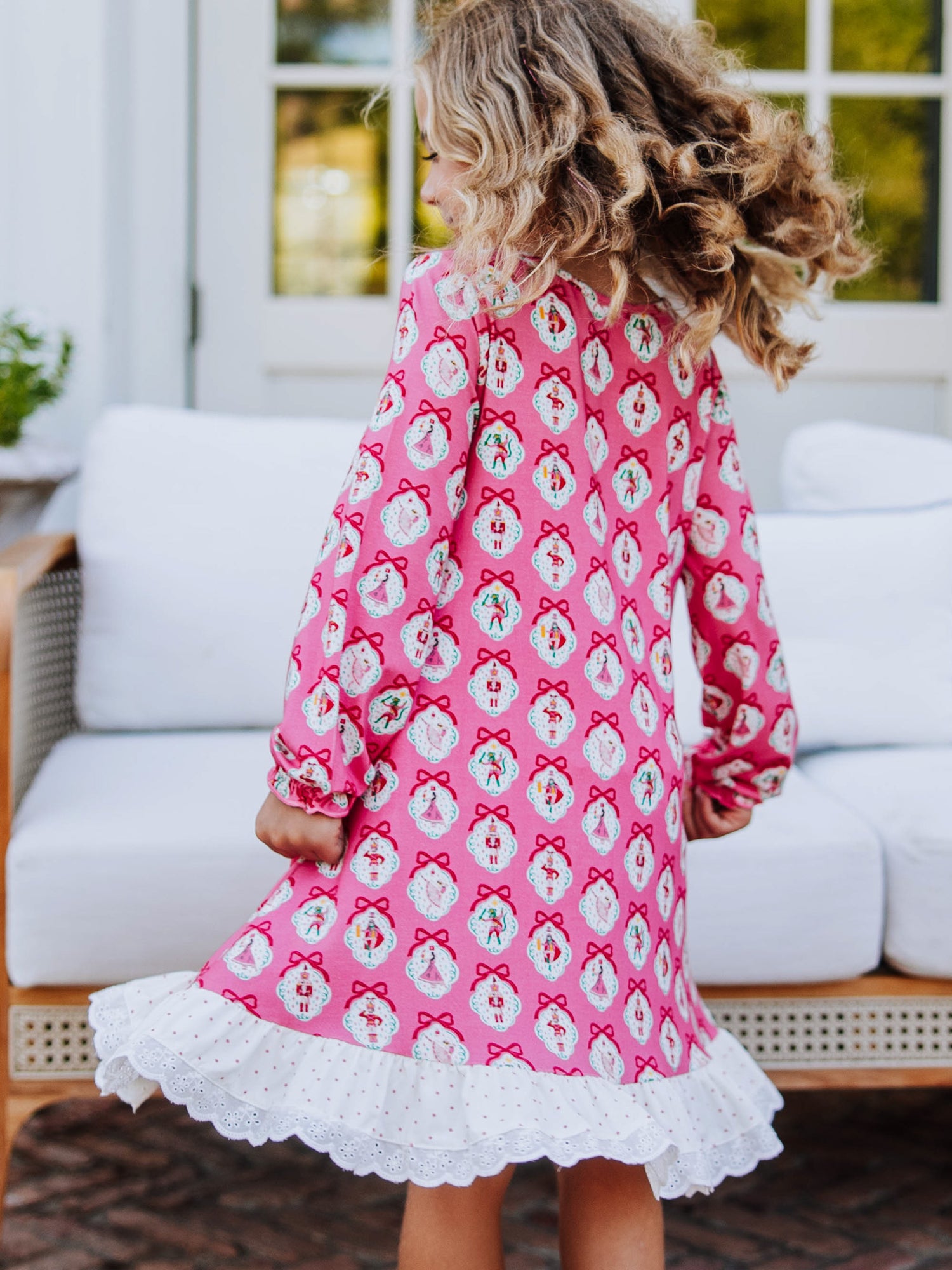 Girl outside wearing a pink nutcracker printed dress. Model is spinning slowly so the dress has movement. 