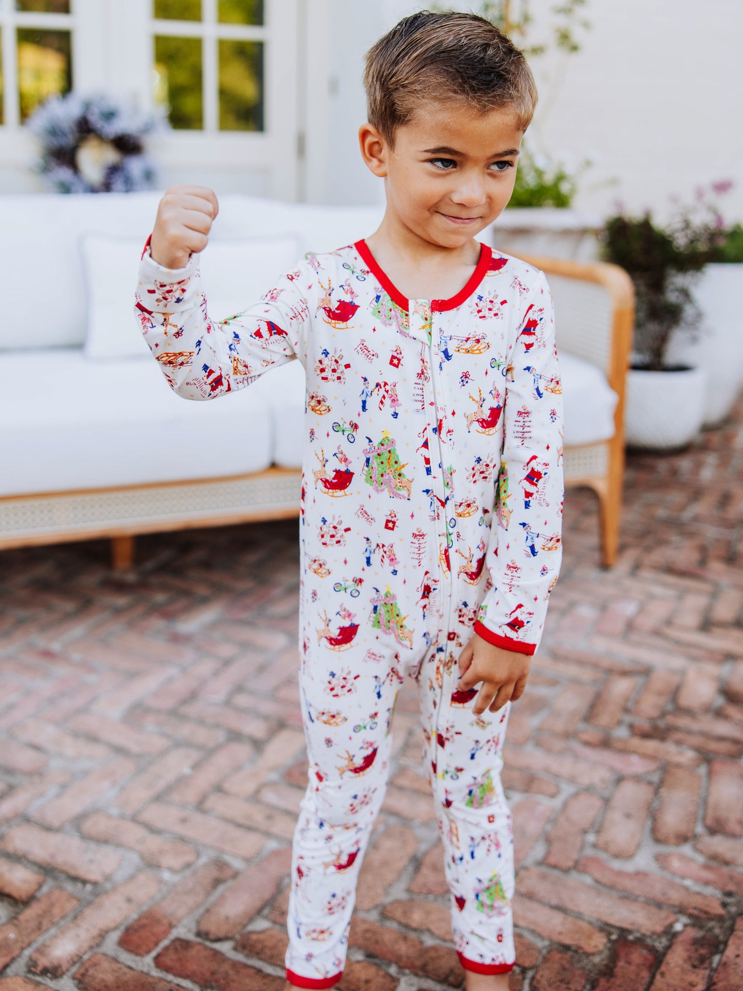 Boy standing on brick outside showing his muscles. Boy is wearing a north pole printed layette. 