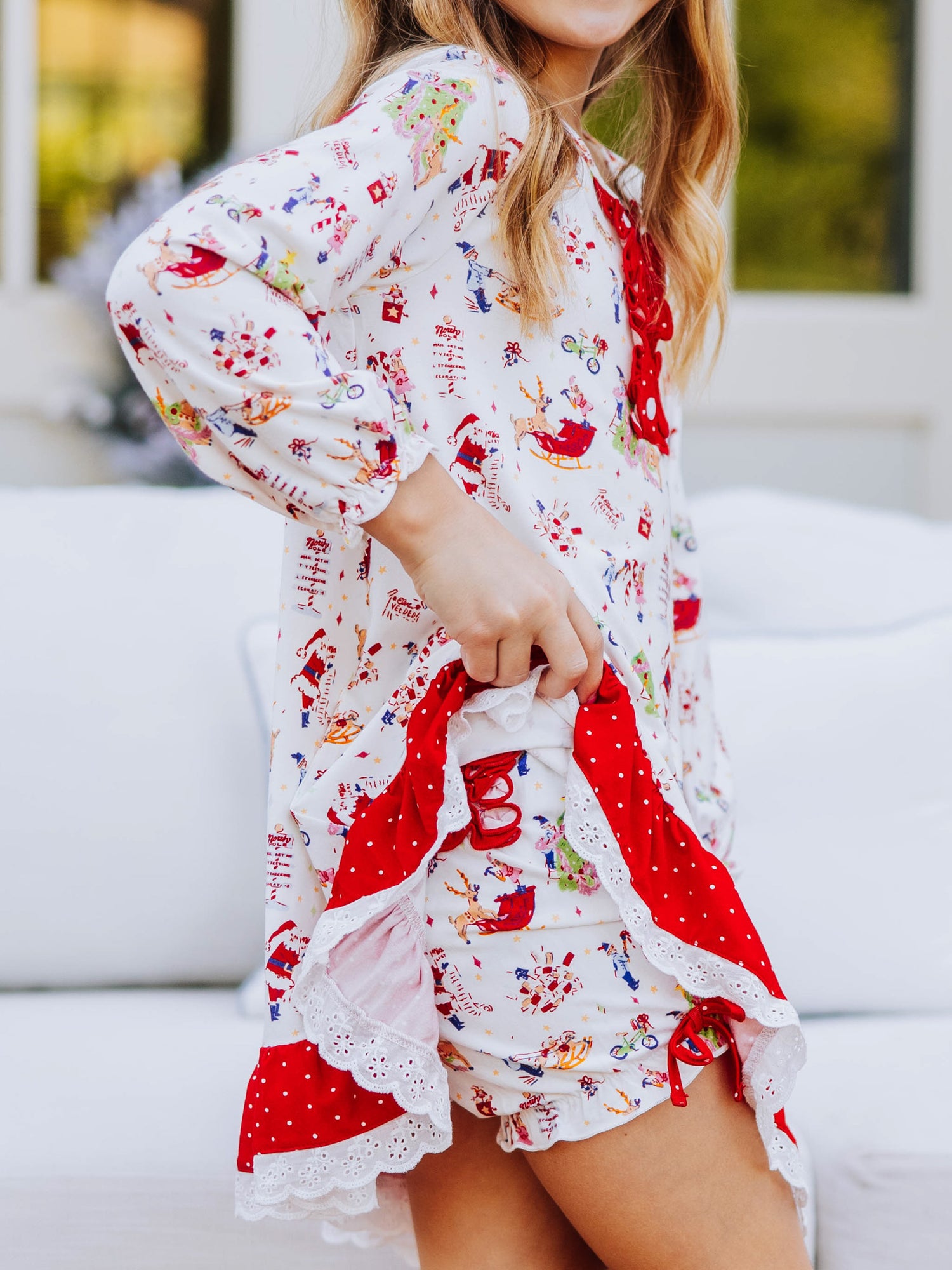 Girl outside wearing a north pole play dress and is holding up one side of the dress to show the matching bloomers underneath