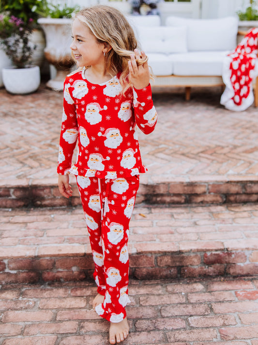 Girl tucking hair behind ear and walking down steps wearing a matching two piece set that is red with white Santa heads.