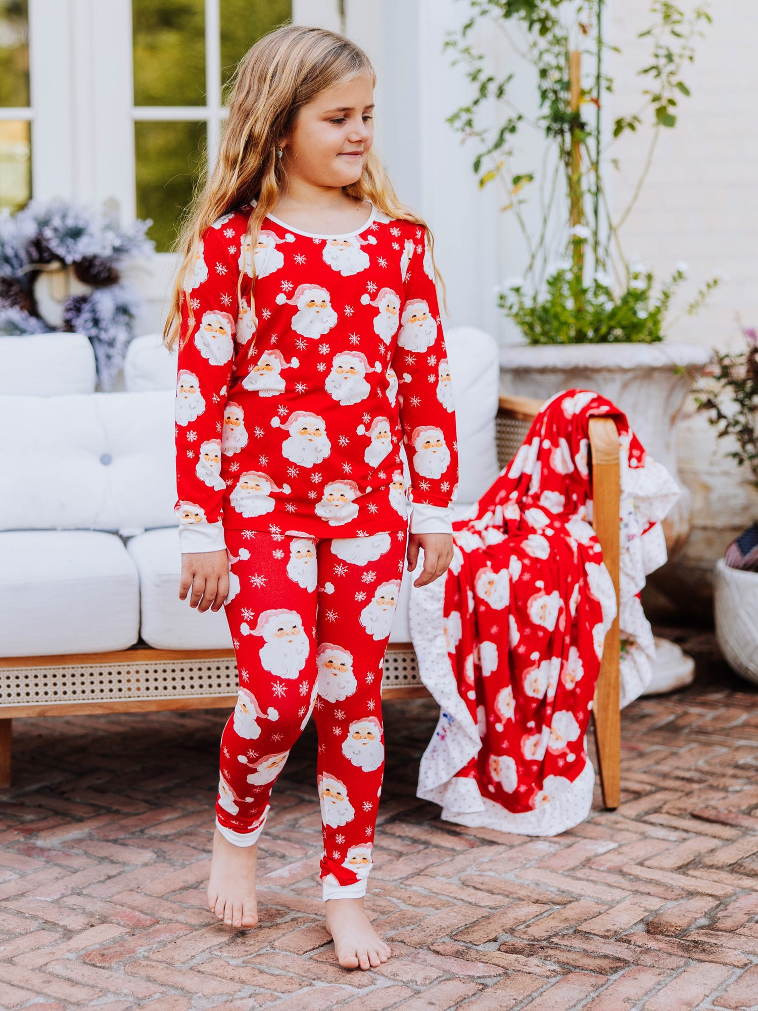 Girl walking outside on brick wearing a red santa pair of fitted pajamas. 