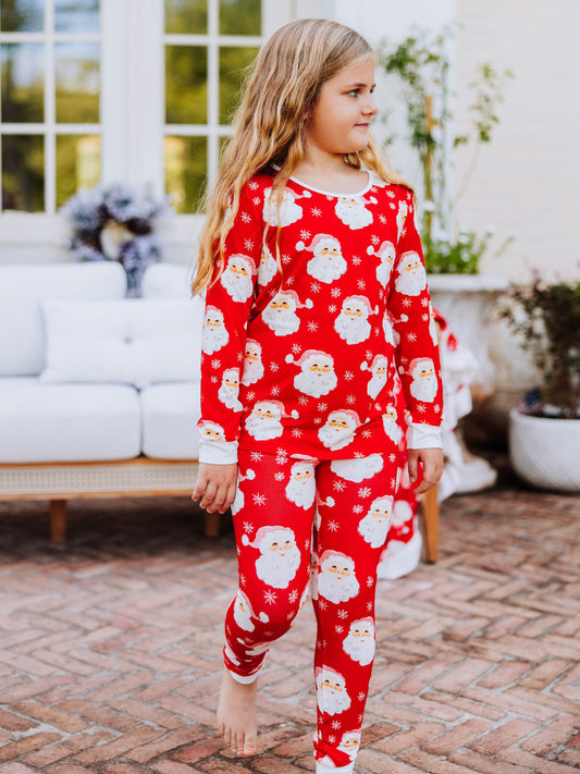 Girl walking outside on brick wearing a red santa pair of fitted pajamas. 