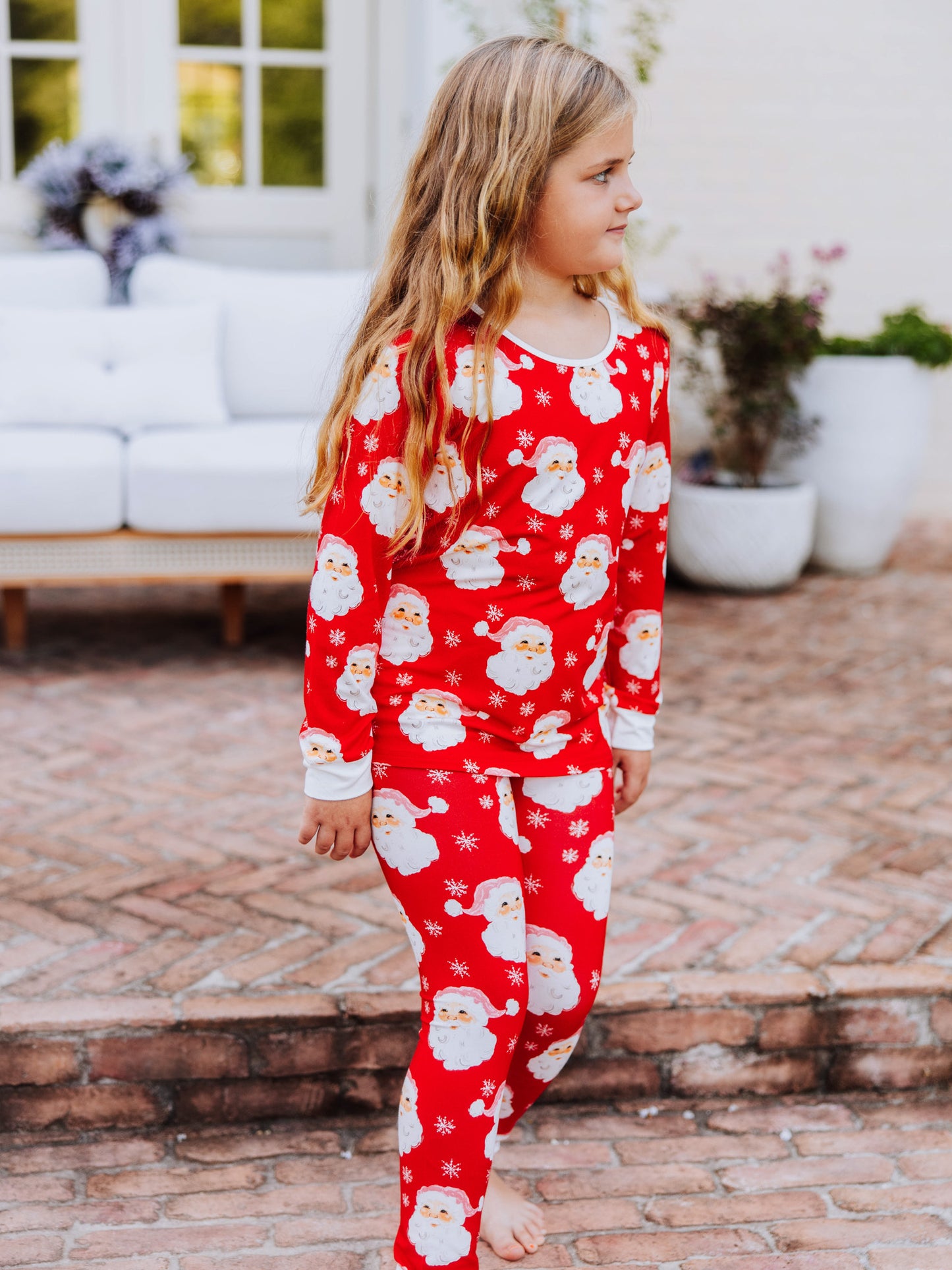 Girl walking outside on brick wearing a red santa pair of fitted pajamas. 
