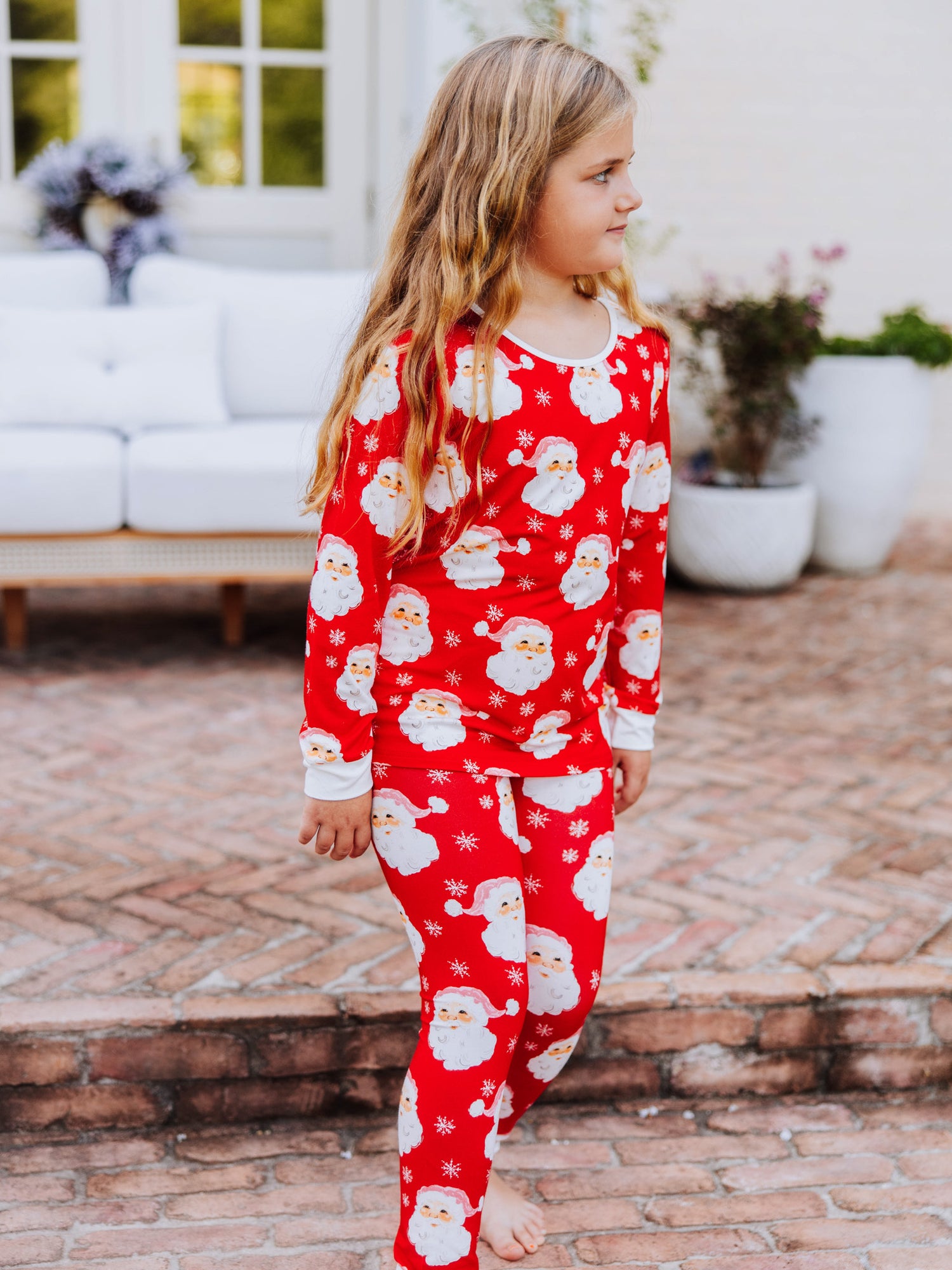 Girl walking outside on brick wearing a red santa pair of fitted pajamas. 
