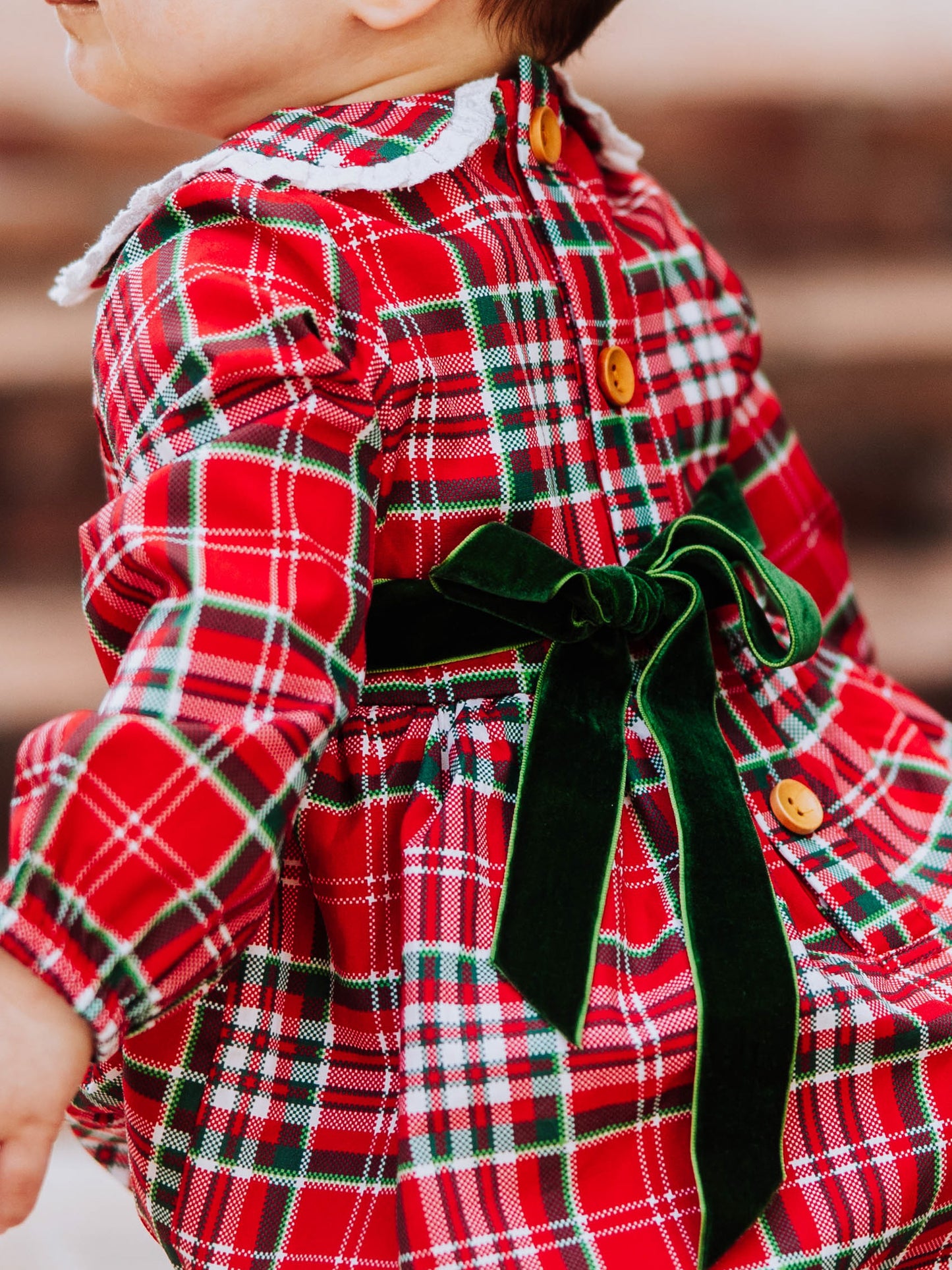 Close up of deep green velvet tie at back of traditional plaid colored bubble with wooden buttons. 