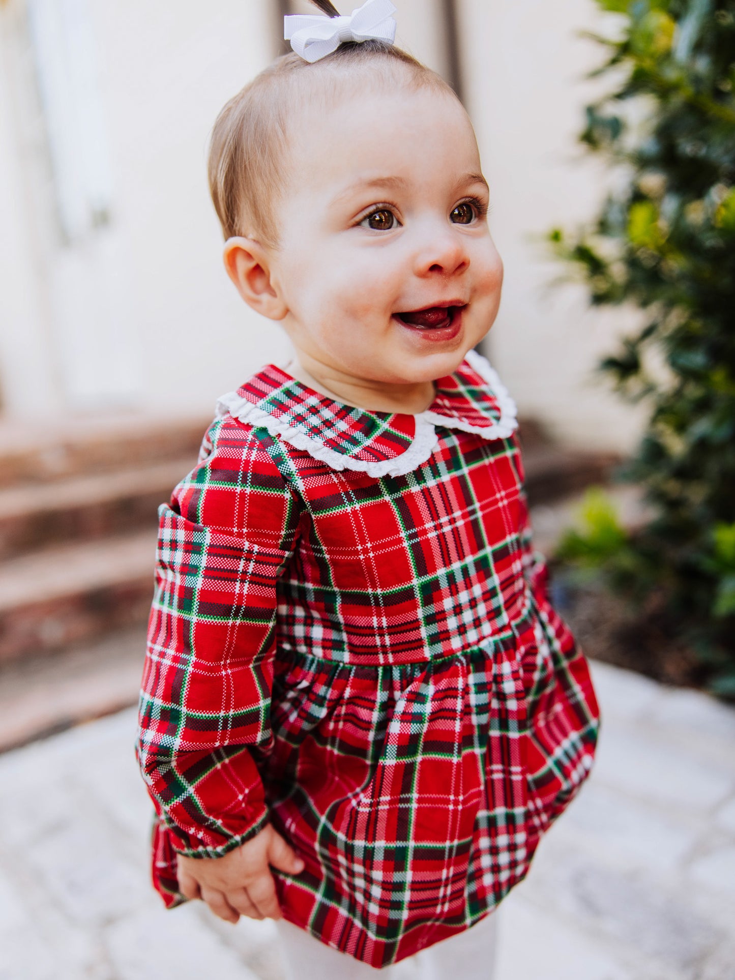 Toddler outside walking on steps in a traditional christmas plaid clothing bubble. Toddler is wearing ivory colored tights. 