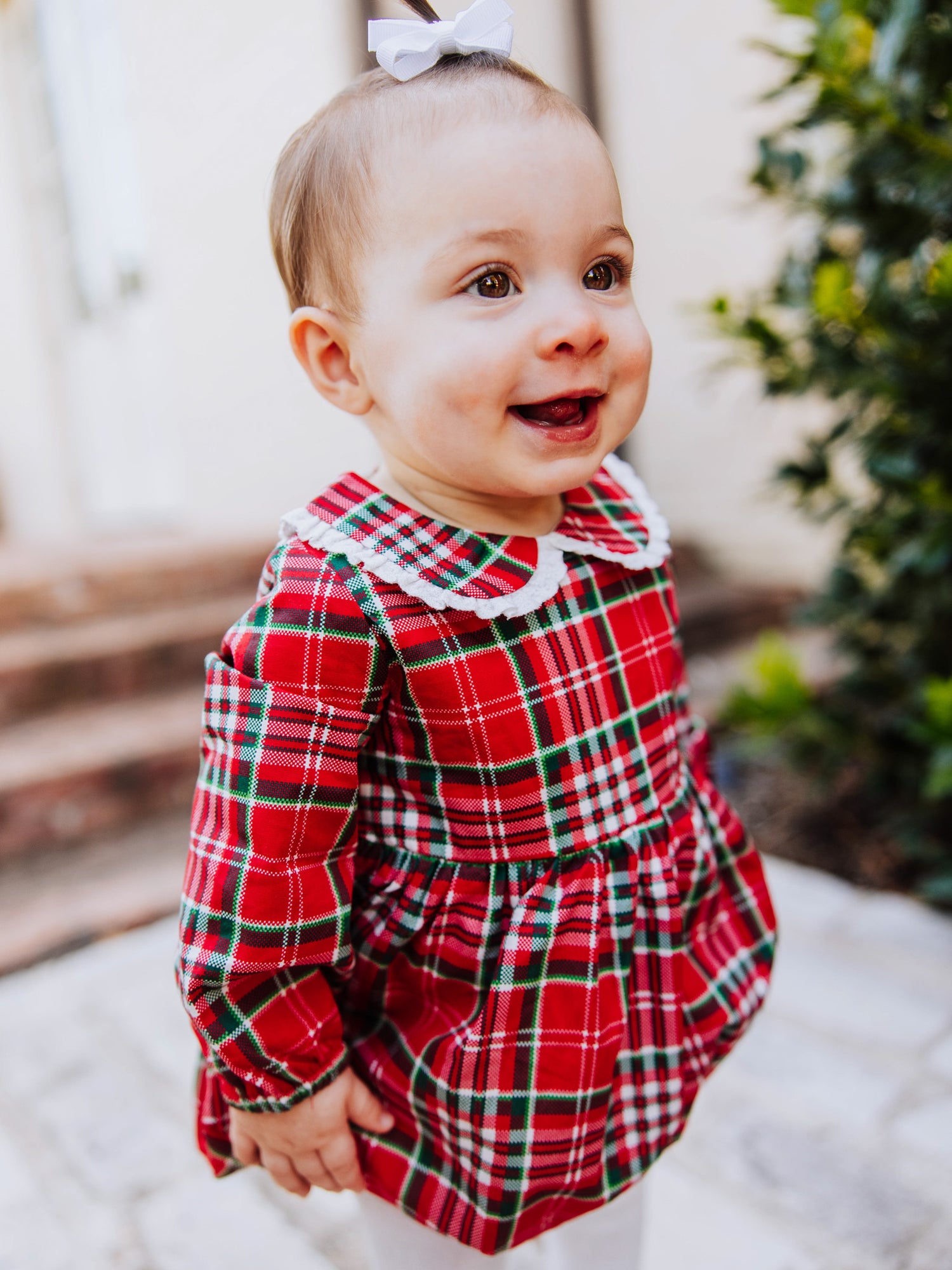 Toddler outside walking on steps in a traditional christmas plaid clothing bubble. Toddler is wearing ivory colored tights. 