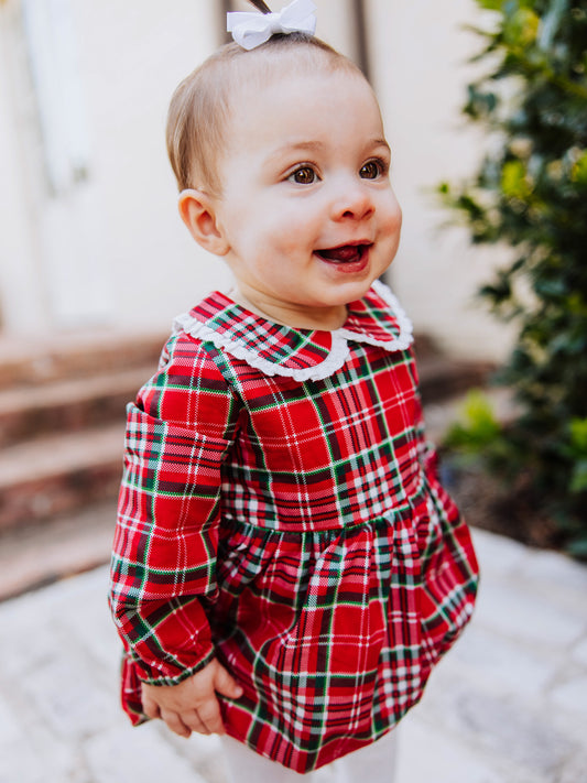 Toddler outside walking on steps in a traditional christmas plaid clothing bubble. Toddler is wearing ivory colored tights. 