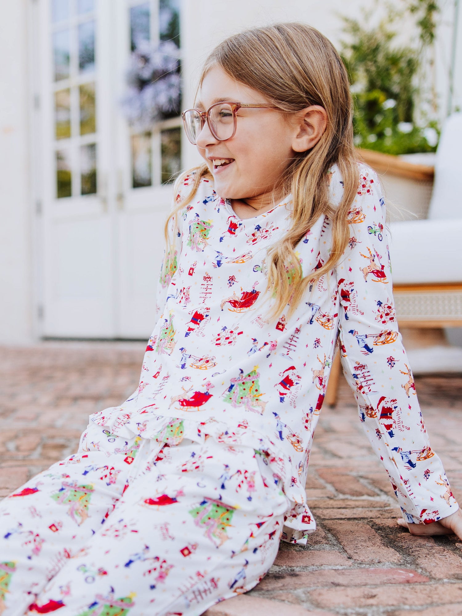 Girl sitting outside on step leaned back and is wearing a north pole pattern ruffled top. 