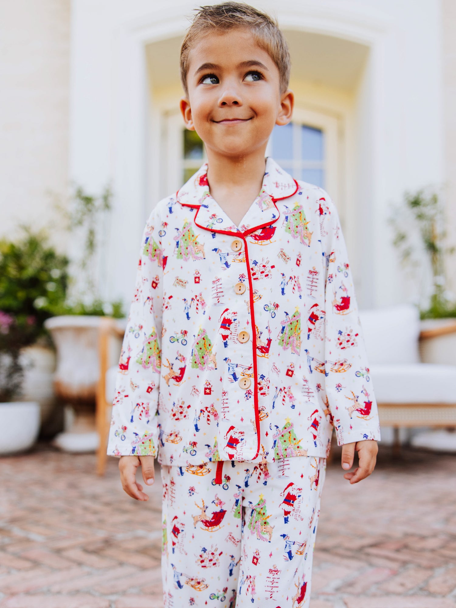 Boy standing outside in front of white couth wearing a christmas pattern button set