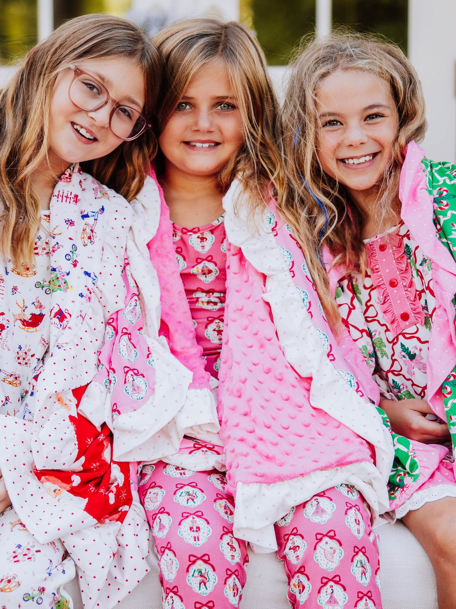 three girls sitting closely all having different printed blankets draped over them