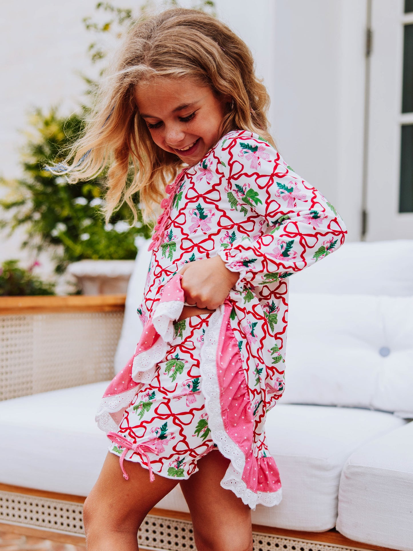 Girl outside wearing a bow printed dress and is holding up the side of it to show the matching bloomers. 