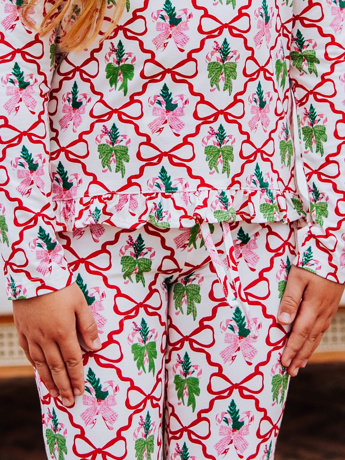 Up close picture of the pattern on a two piece set. The top and bottom have red bows throughout along with some pink and green bow designs. 
