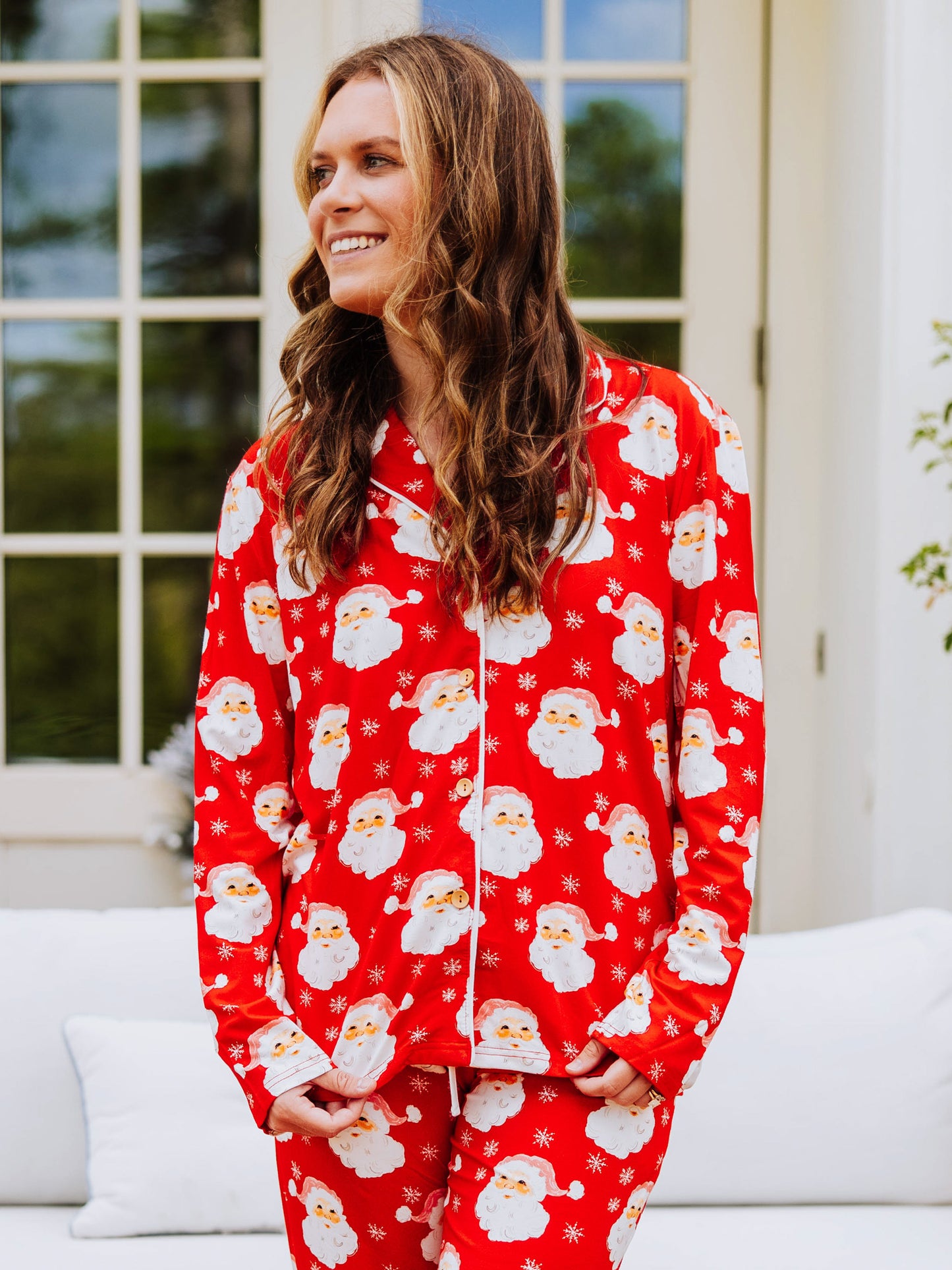 Women standing outside in front of a couch wearing button-up, red santa pajamas
