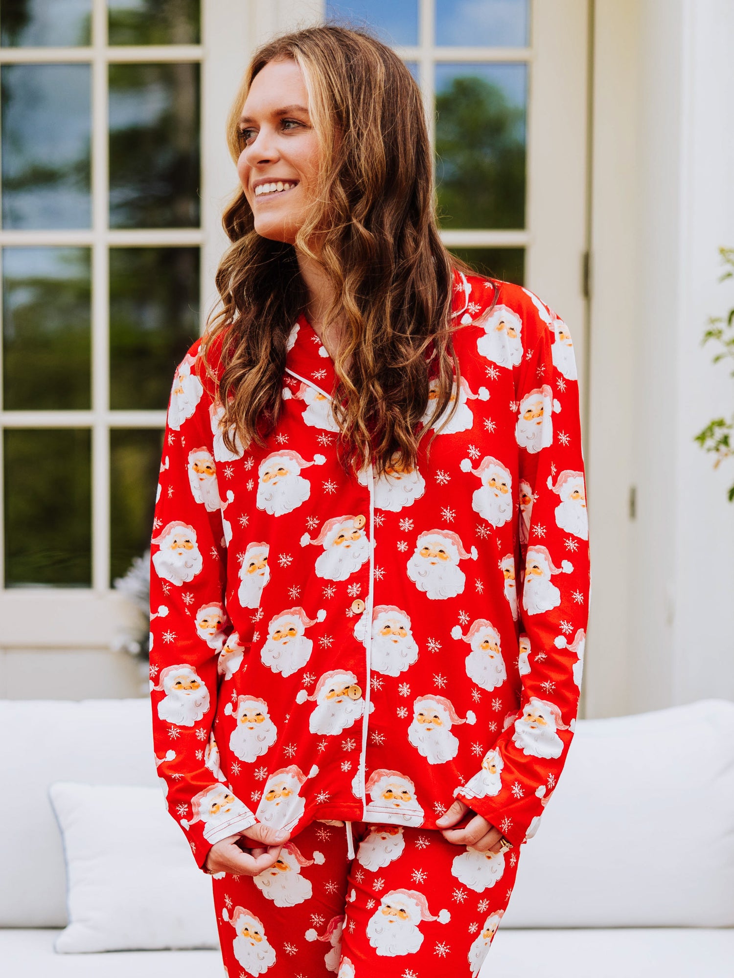 Women standing outside in front of a couch wearing button-up, red santa pajamas