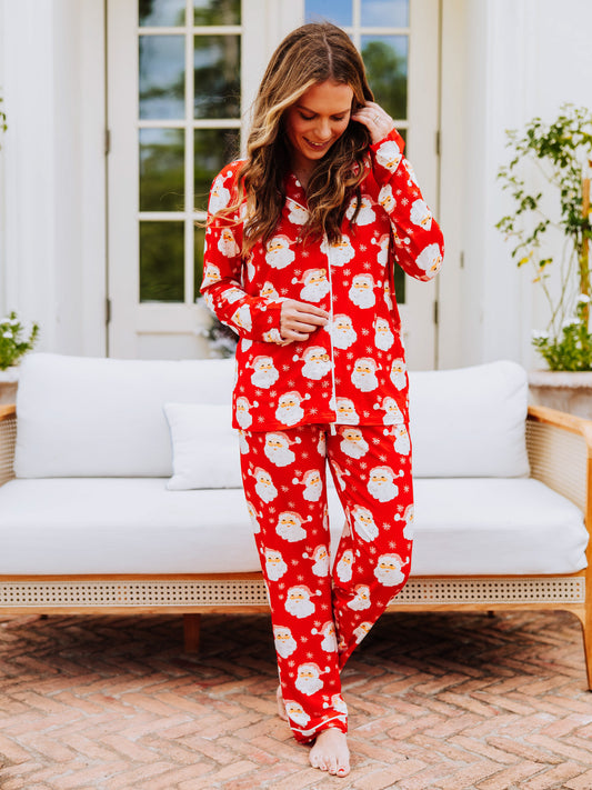 Women standing outside in front of a couch wearing button-up, red santa pajamas. Girl is looking down at buttons