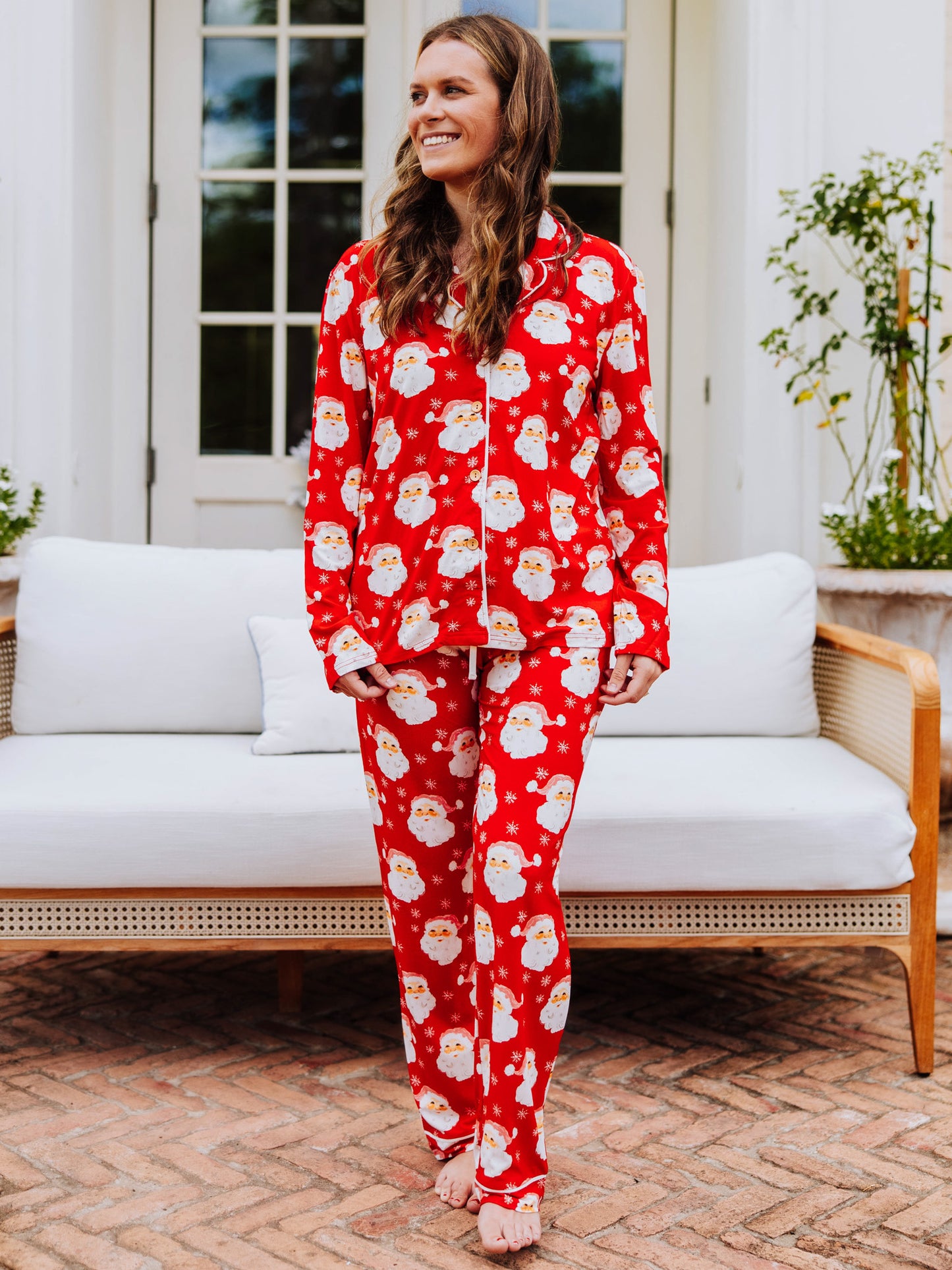 Women standing outside in front of a couch wearing button-up, red santa pajamas
