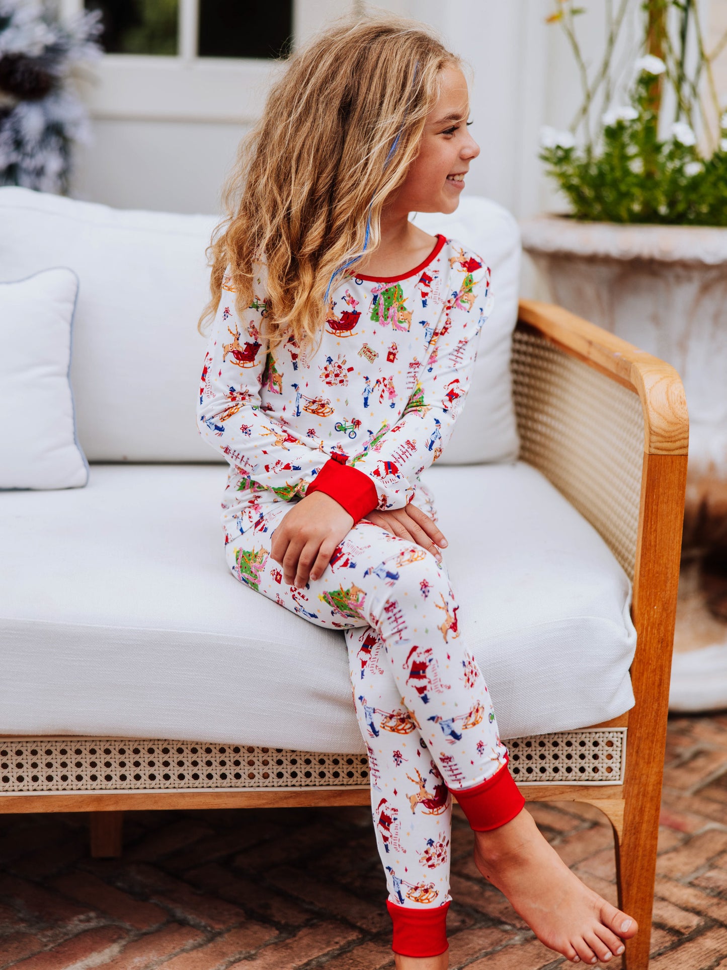 Girl sitting outside on a white couch with legs crossed. She is wearing a pair of fitted pajamas with a north pole print. 