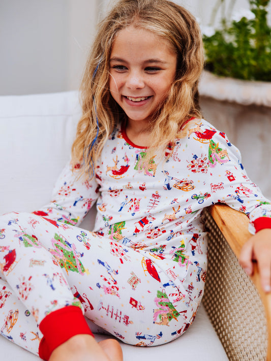 Girl standing with feet crossed outside in front of white couch. Model is wearing a fitted pair of pajamas with a north pole print. 