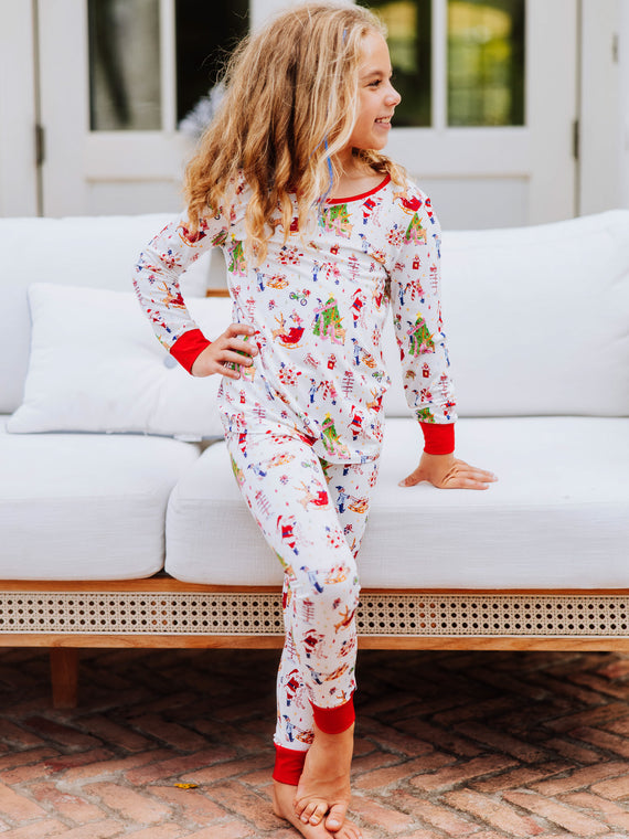 Girl standing with feet crossed outside in front of white couch. Model is wearing a fitted pair of pajamas with a north pole print. 