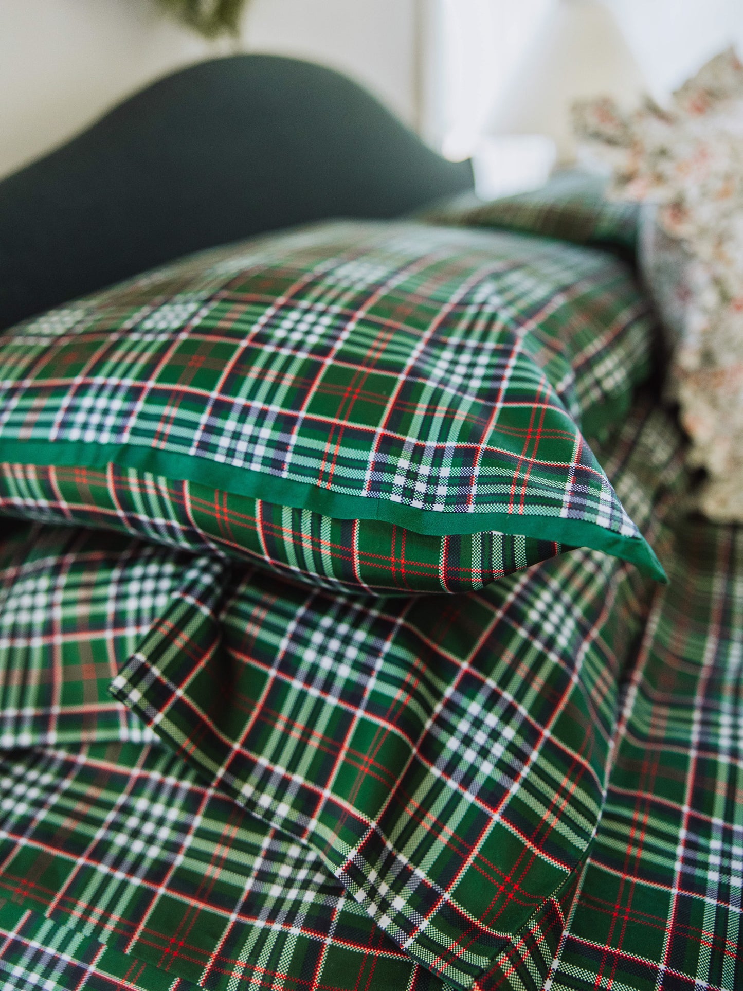Up close picture of traditional green plaid pillow cases with solid green piping on one of the pillow.