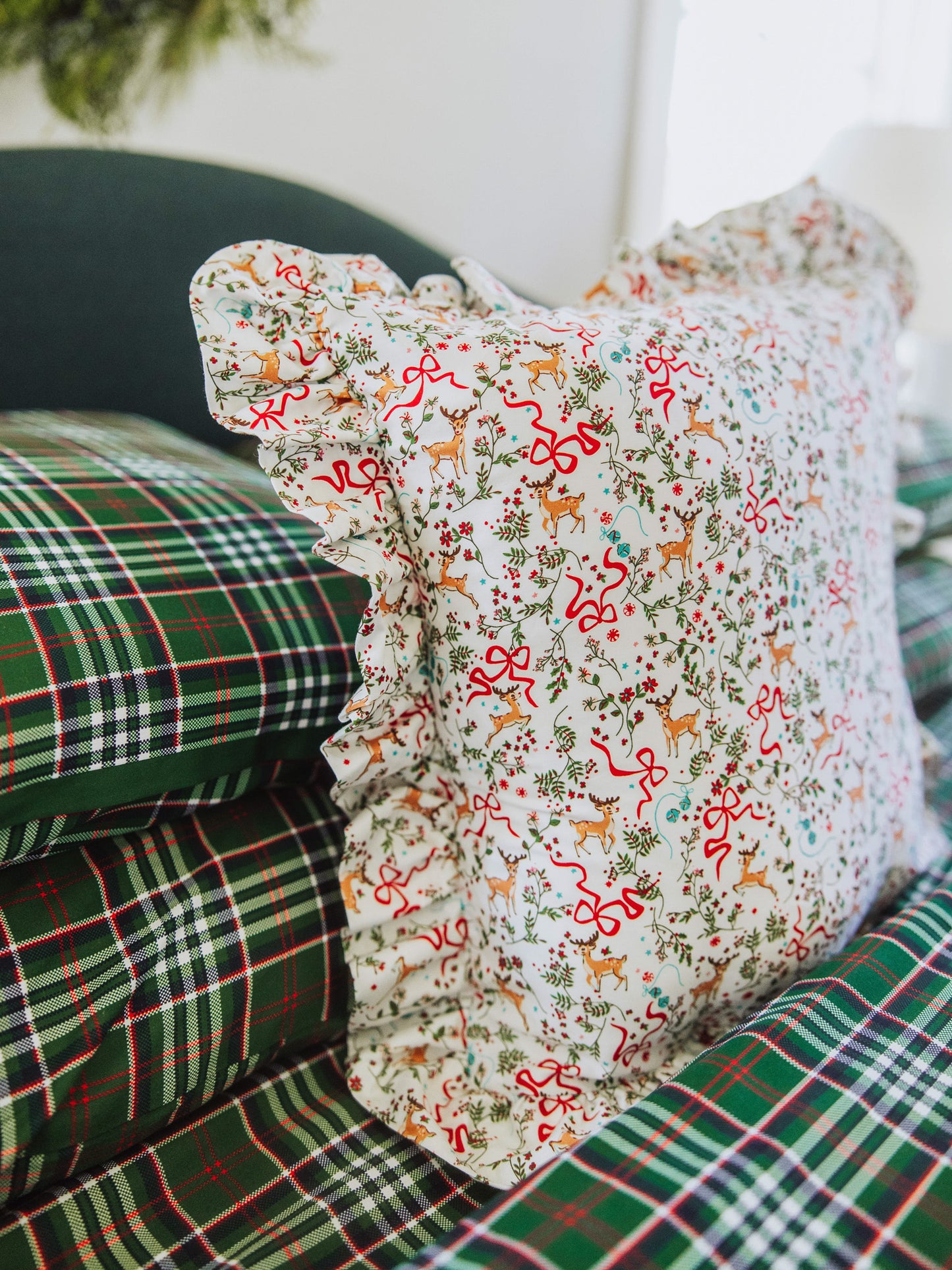 Christmas themed pillow shown with traditional green plaid bedding and other pillows.