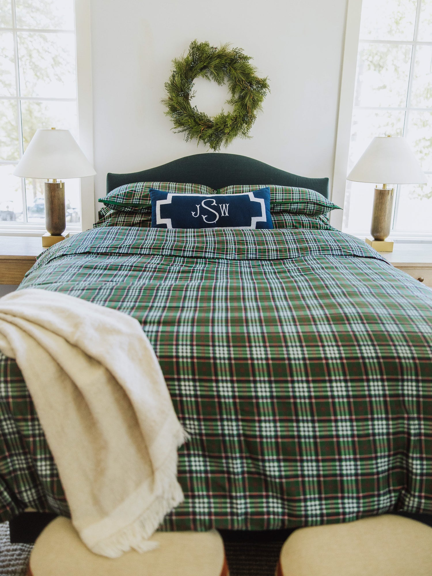 Traditional green plaid made bed with throw blanket at corner of bed. Decorative navy pillow in the middle. 