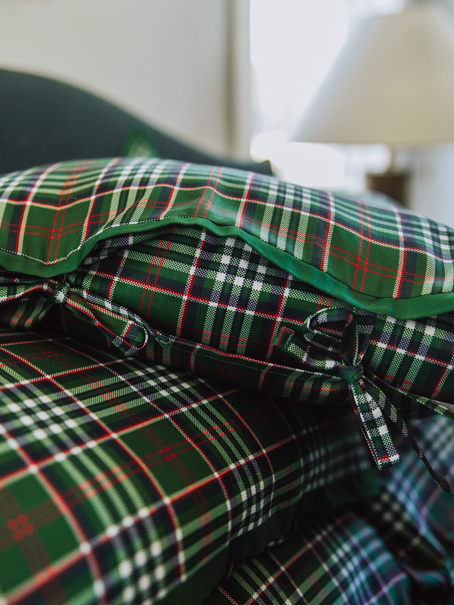 Up close picture of traditional green plaid pillow cases with tie closures and  solid green piping on one of the pillow.