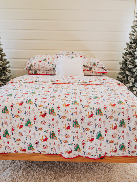 Matching Christmas bedding and a 16x16 white pillow in the middle. Christmas trees on each side of bedding.
