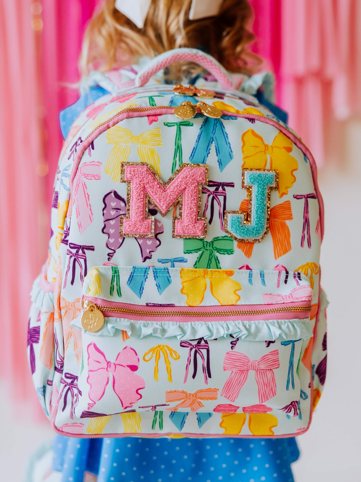 Girl wearing backpack with vibrant colored bows that has multi-colored patches on front.