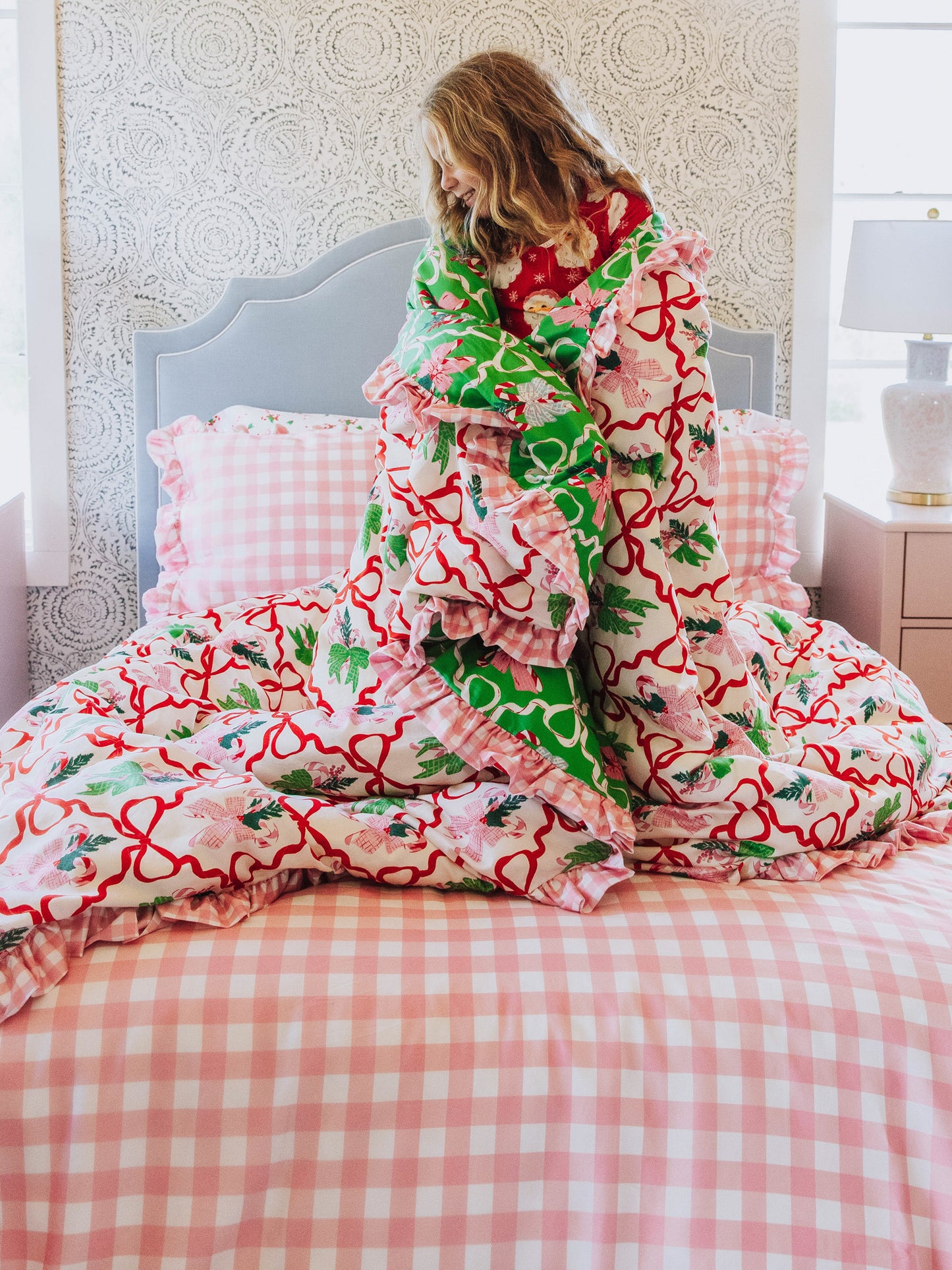 Girl standing on pink gingham bedding wrapped up in a Christmas themed duvet. 