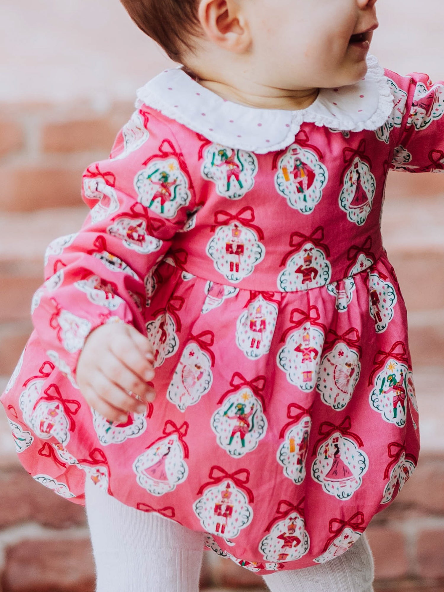 Baby girl outside wearing apink nutcracker print classic bubble with white tights and black mary janes. 