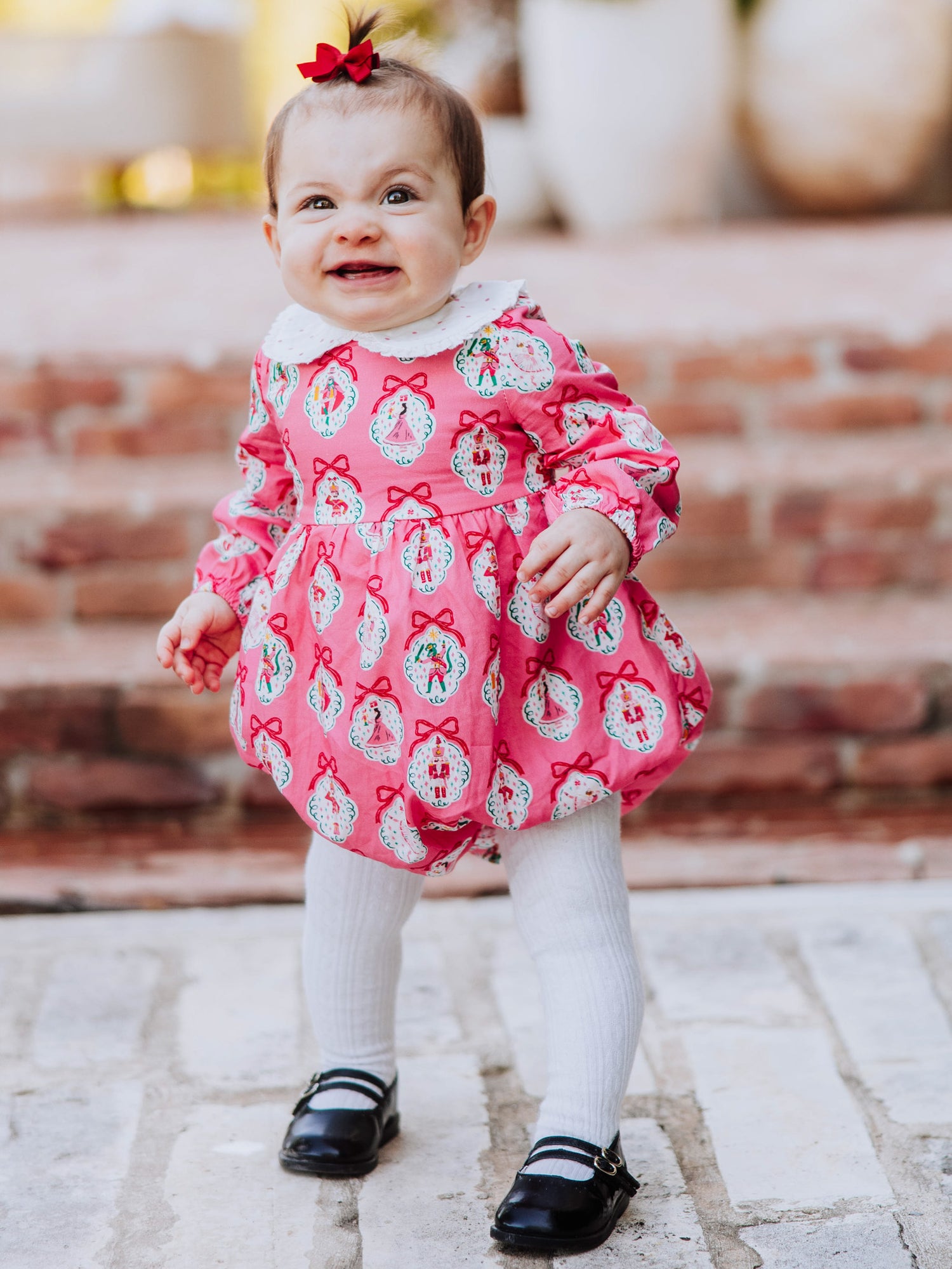Baby girl outside wearing apink nutcracker print classic bubble with white tights and black mary janes. 