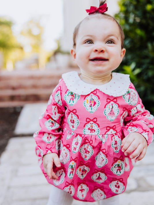 Baby girl outside wearing apink nutcracker print classic bubble with white tights and black mary janes. 