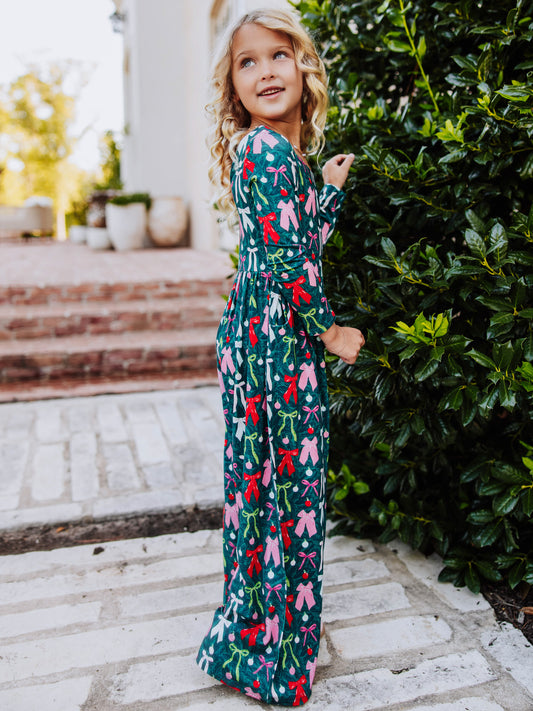 Model standing next to greenery wearing a multi colored bow printed leggy romper. 