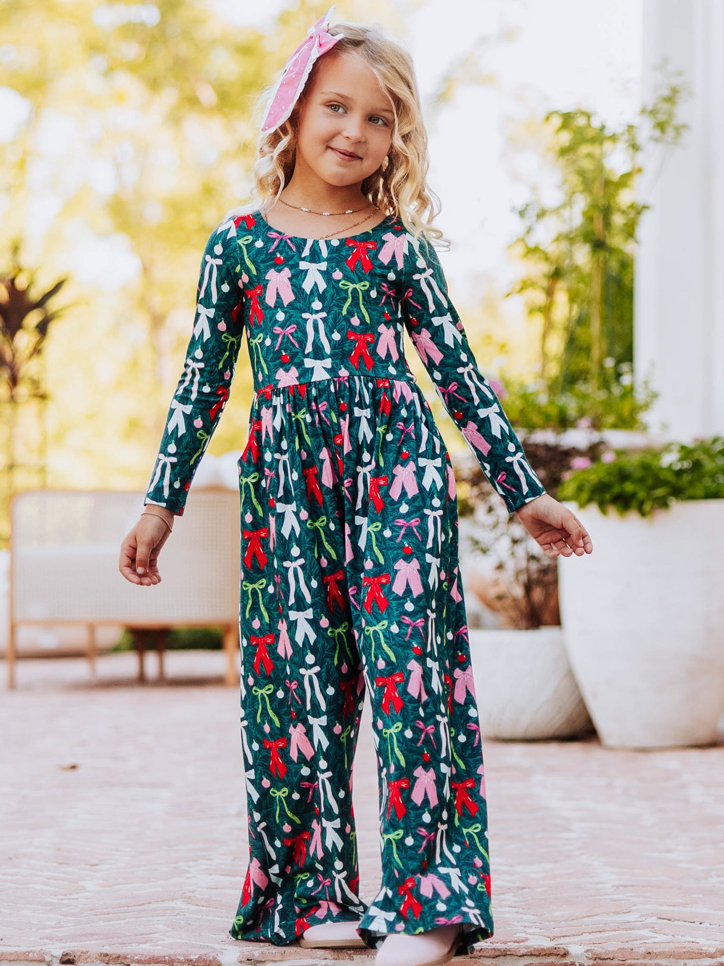 Model standing on steps with arms out wearing a colorful bow leggy romper. 
