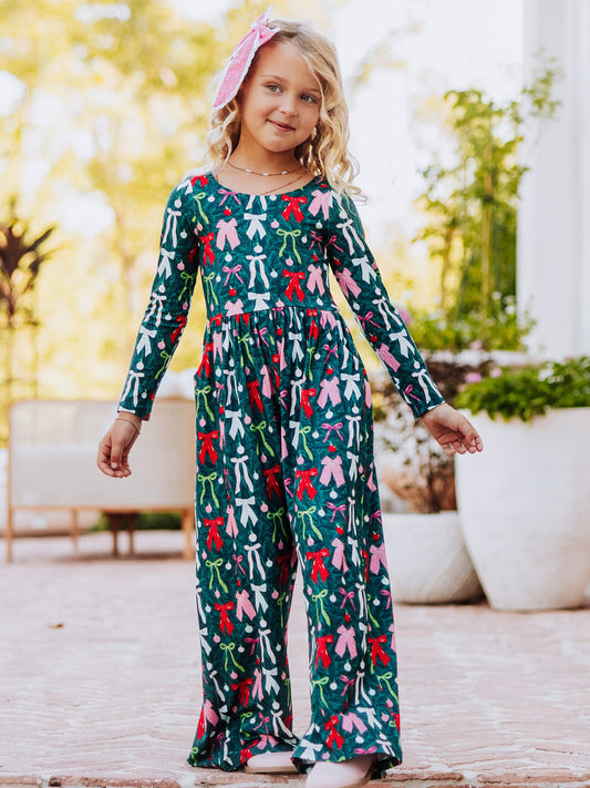 Model standing on steps with arms out wearing a colorful bow leggy romper. 