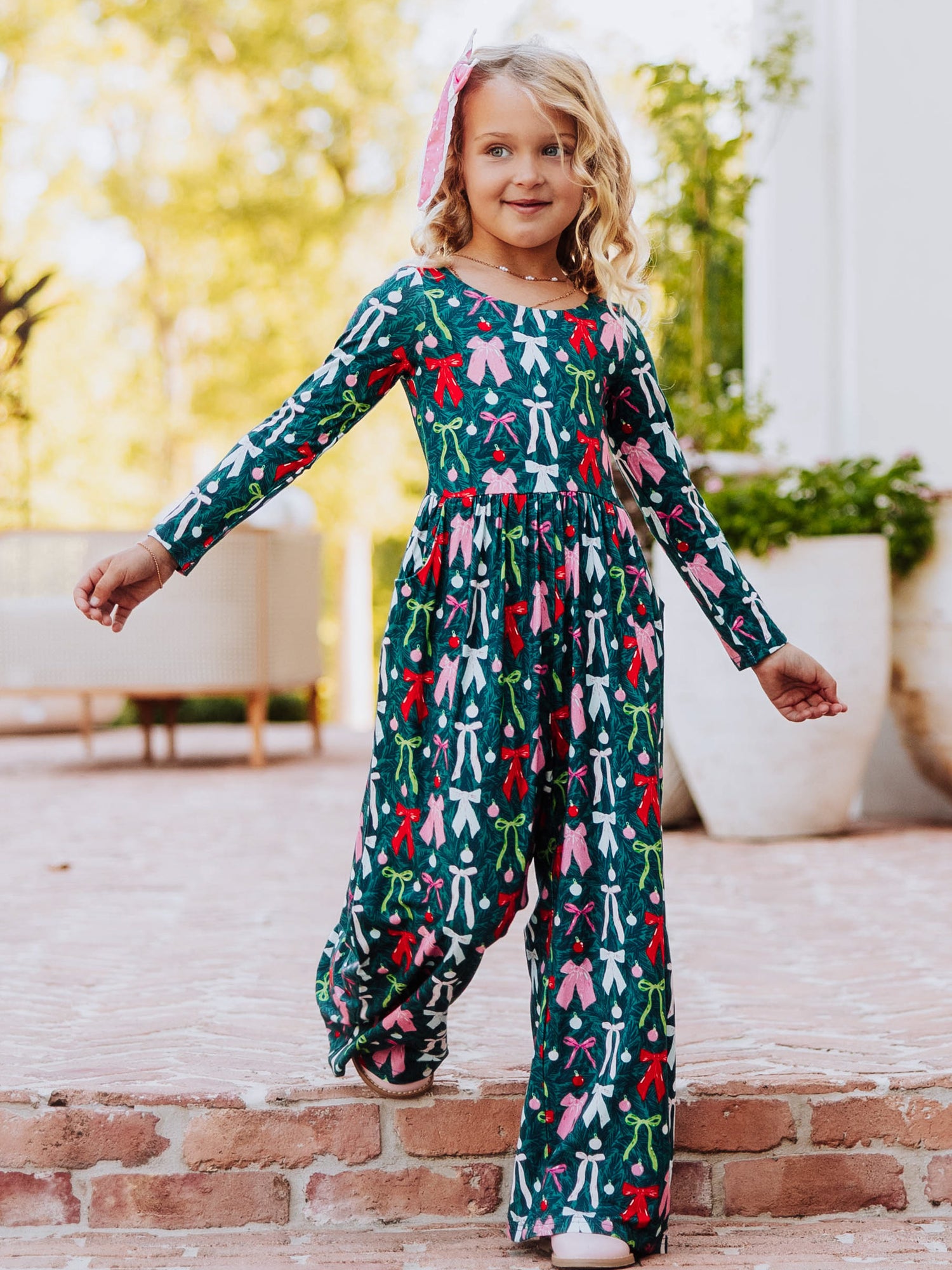 Model walking down steps wearing a multi colored bow patterned leggy romper. 