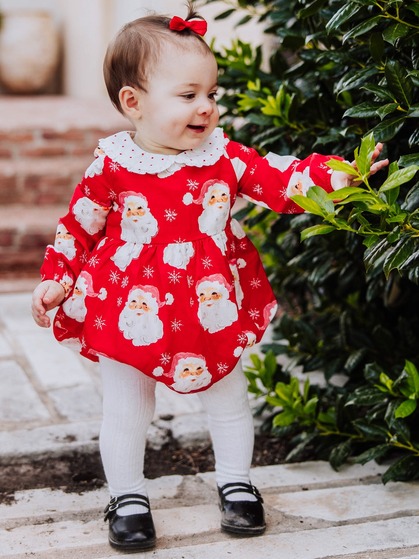 Baby girl outside wearing a jolly santa print classic bubble with white tights and black mary janes. 