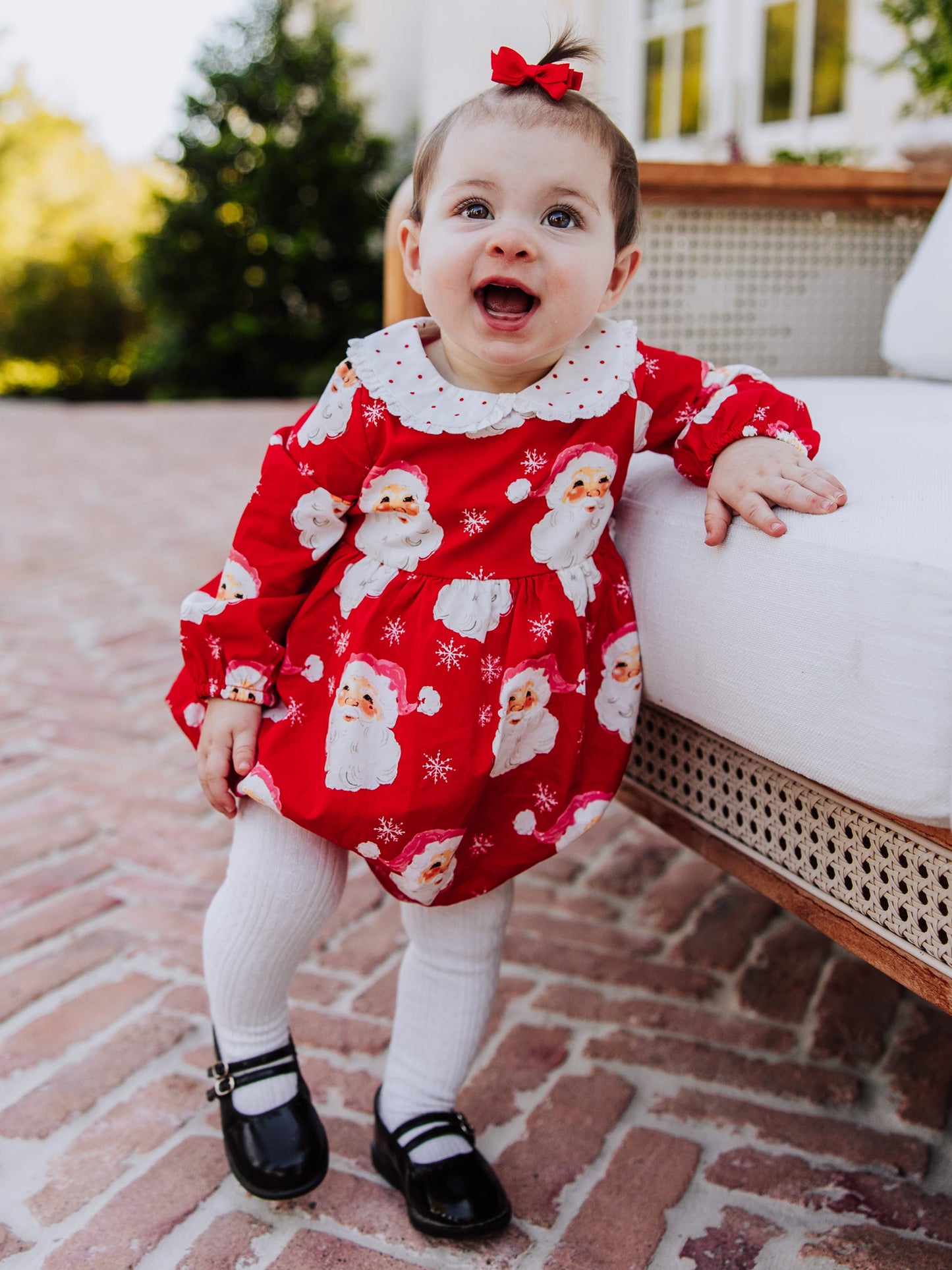 Baby girl outside wearing a jolly santa print classic bubble with white tights and black mary janes. 