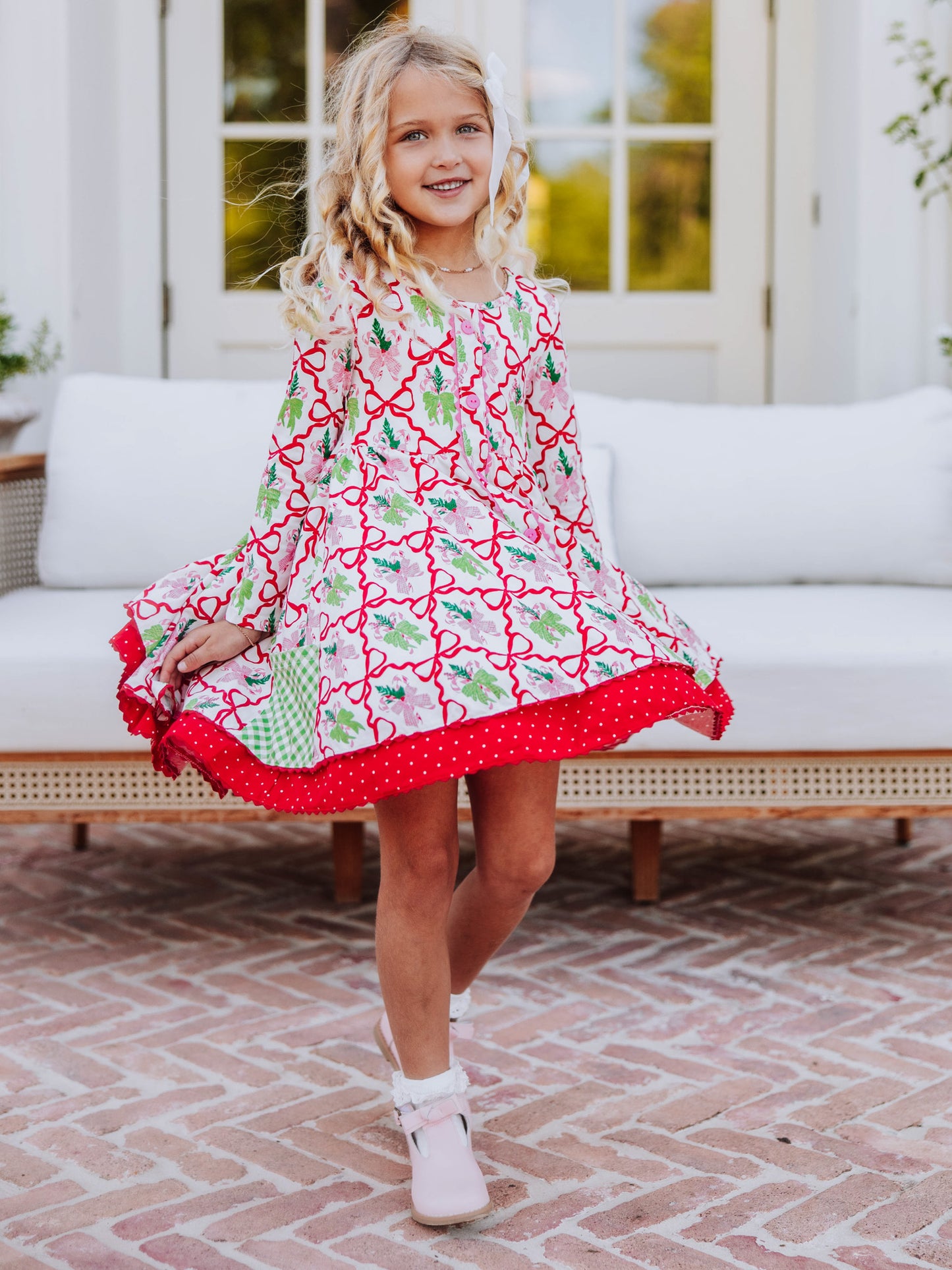Girl standing outside holding both sides of dress. Dress is a holiday bow printed pattern with double layers. 