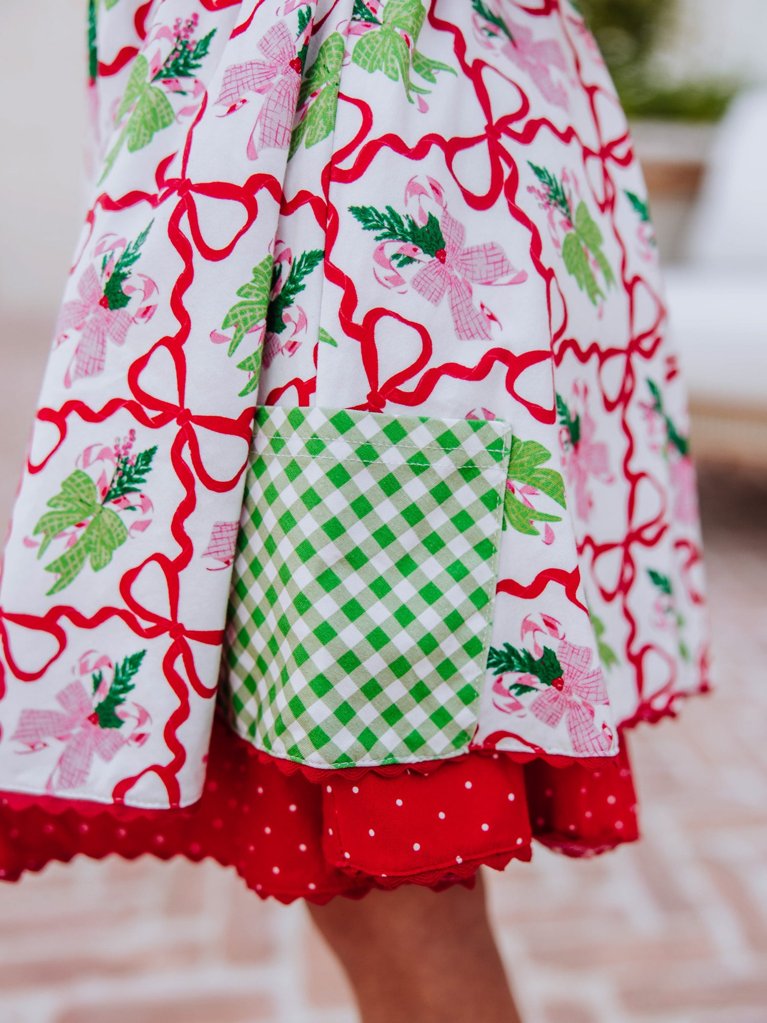 Up close shot of holiday bow printed dress and green gingham accent pocket on side of dress. 