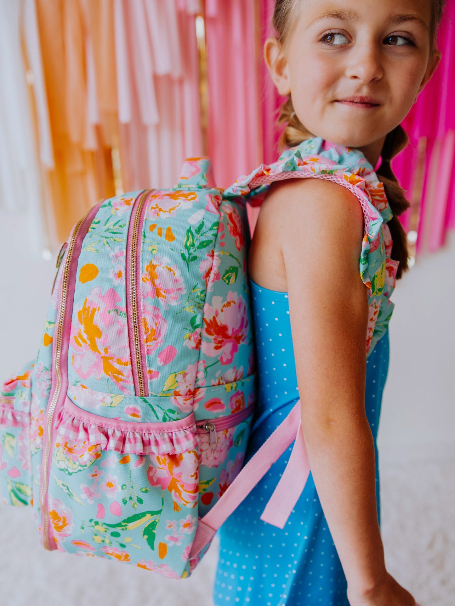 Picture of girl in blue outfit wearing a colorful and floral backpack. Picture is a side proffile