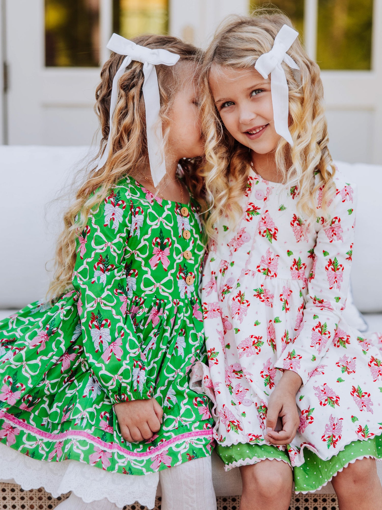 Two girls sitting next to one another. Both are wearing holiday themed dresses. 