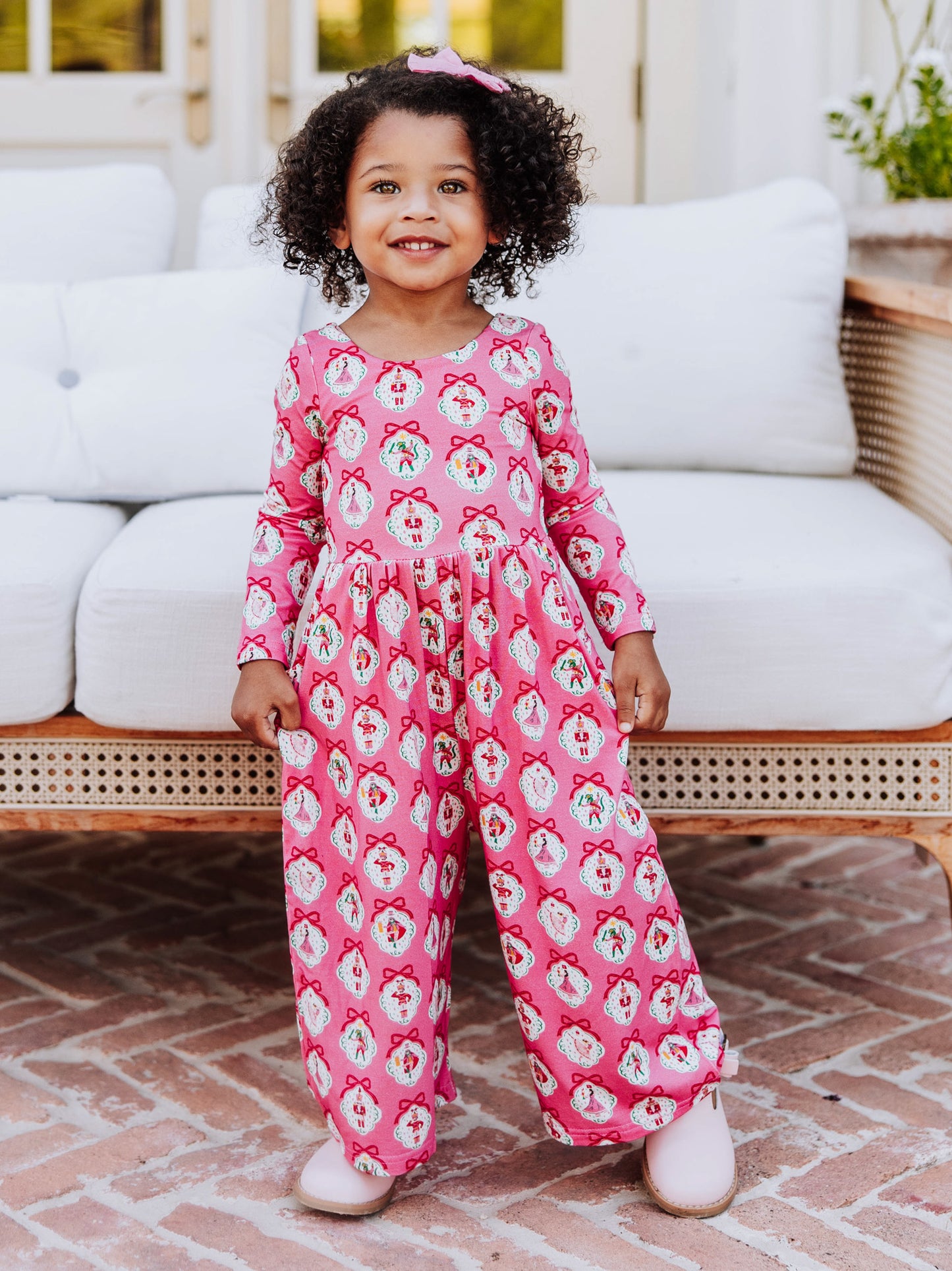 Girl standing in front of white couch wearing a pink nutcracker printed leggy romper.