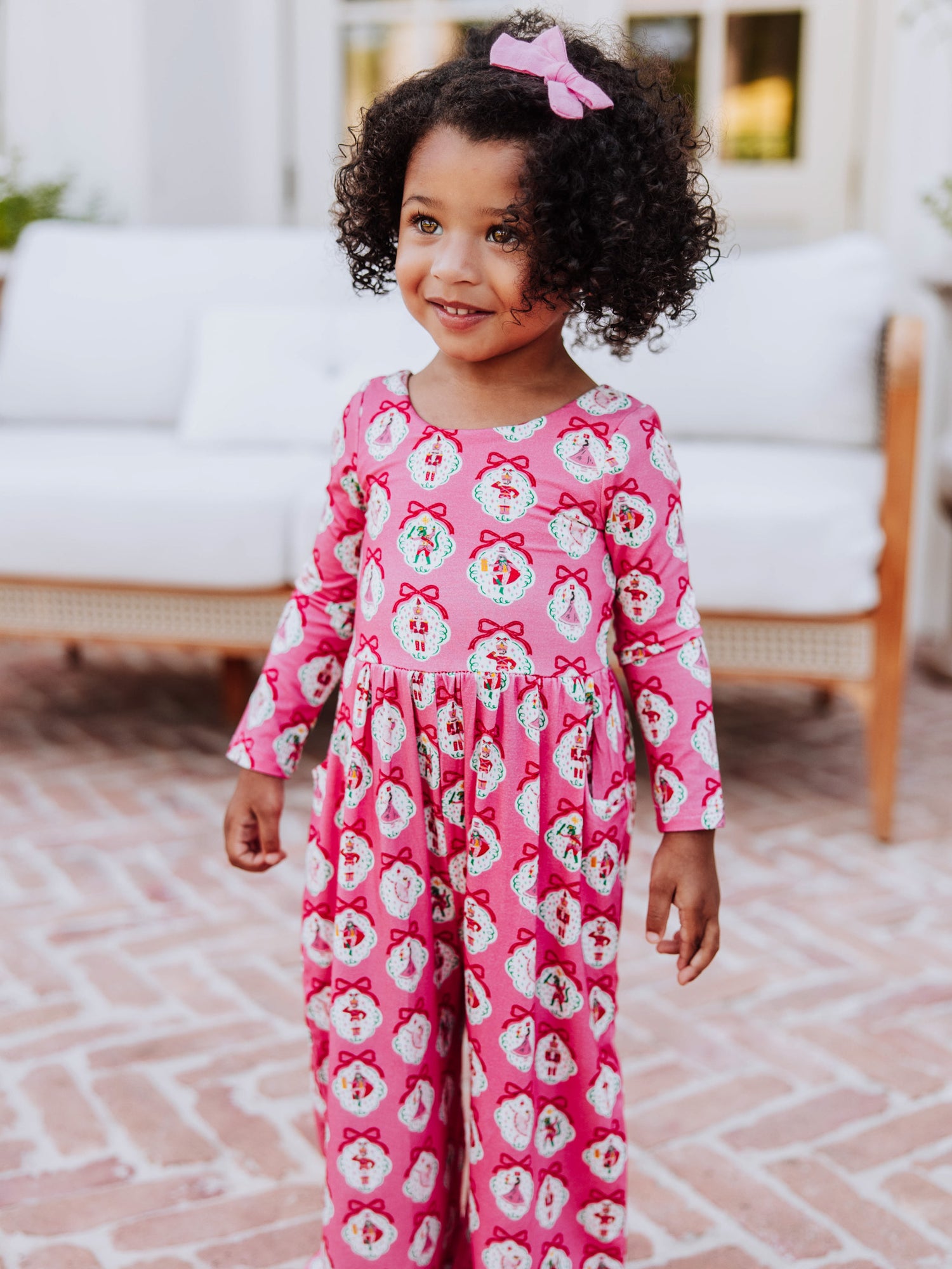 Girl standing in front of white couch wearing a pink nutcracker printed leggy romper.