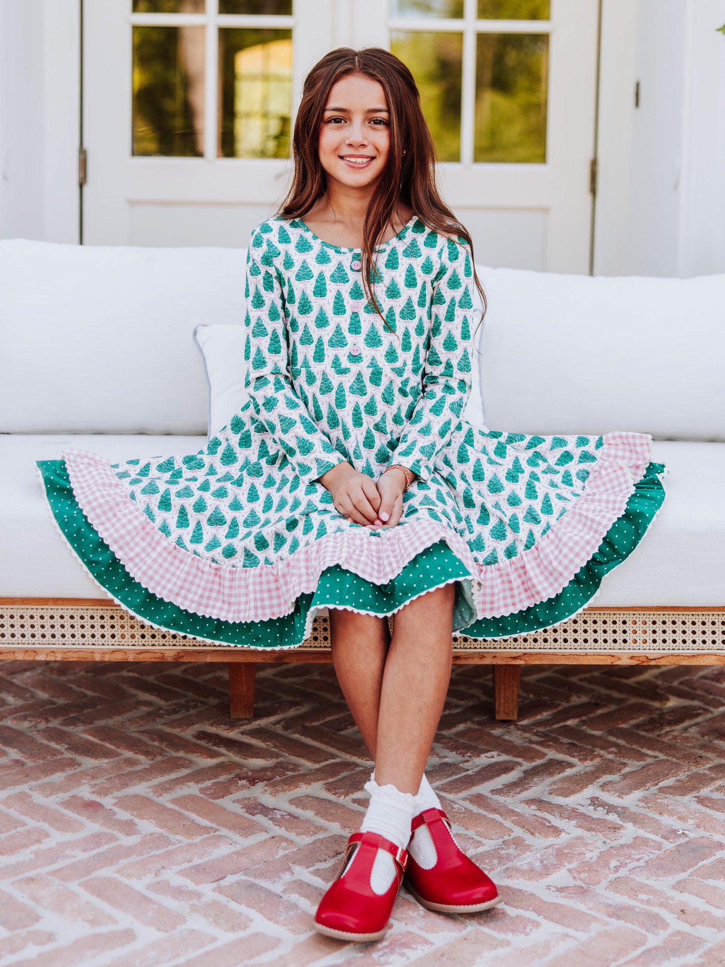 Girl sitting on white couch wearing Christmas themed dress and red mary janes