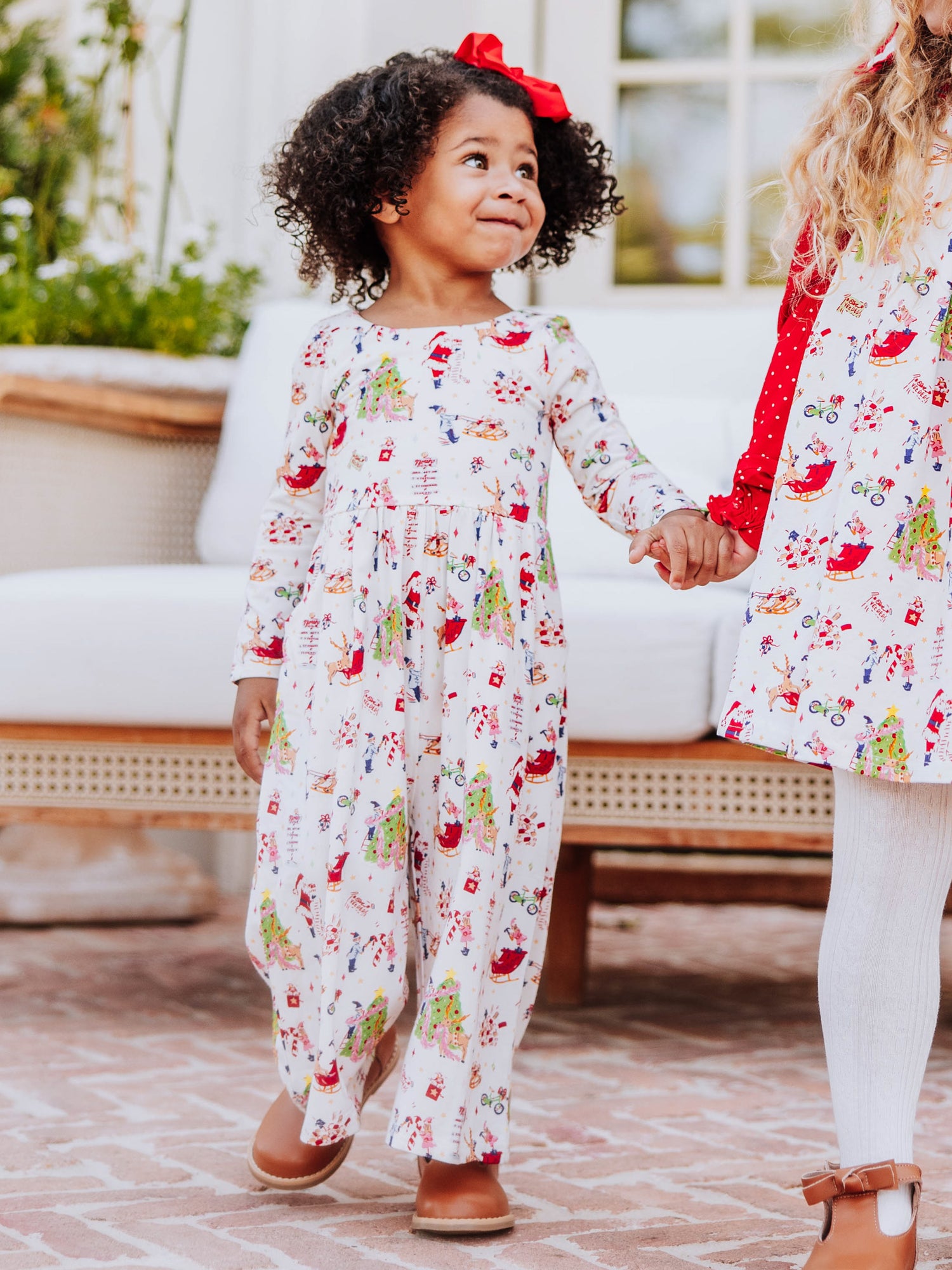 Two girls holding hands both wearing north pole printed clothing. 