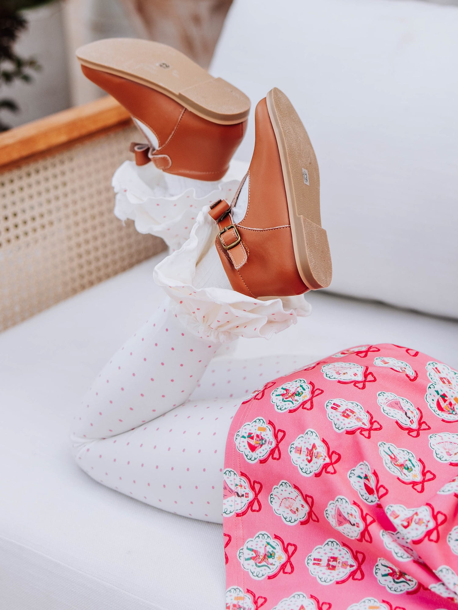 Girl laying down with feet crossed at ankles. She's wearing brown buckle shoes with white leggings with pink polka dots.