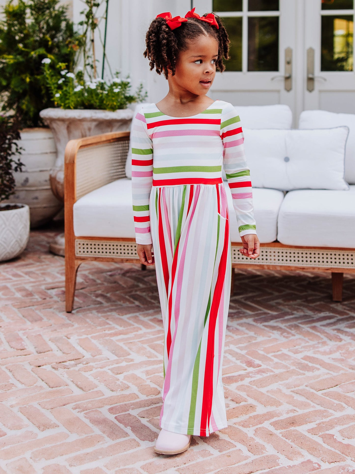 Girl looking off to the side standing in front of a white couch outside wearing a multi striped leggy romper. 